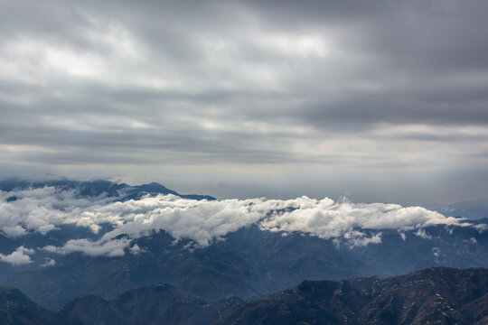 View of majestic mountains cloaked in ethereal white clouds beneath a somber, overcast sky creating a serene yet dramatic vista, Muzaffarabad, Azad Kashmir, Pakistan.
