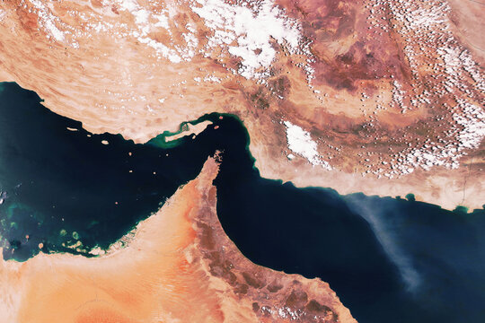 Satellite view of the Strait of Hormuz, connecting the Persian Gulf and Gulf of Oman. High-resolution orbital image featuring arid desert landscapes, deep blue waters, and scattered clouds.