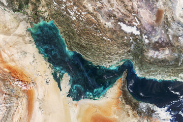 Satellite view of the Persian Gulf showcasing turquoise waters, swirling plankton blooms, and the rugged desert coastlines of the Middle East. High-contrast aerial photography of Earth.
