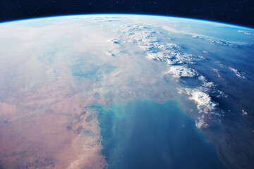 Stunning cinematic view of Earth from space, showing the planet's curvature, thin blue atmosphere, and swirling white clouds over vast desert terrain and deep blue oceans under a starry sky.