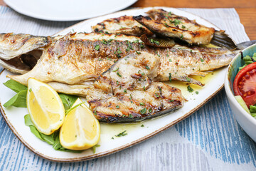Grilled fish served on plate with lemon and herbs. Delicious seafood dish presented with fresh...