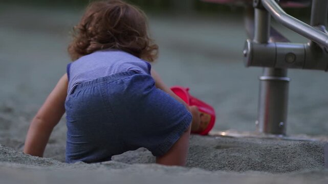 Toddler stepping into sandbox walking with unstable steps then stumbling falling and getting up again before sitting on playground digger capturing resilience and playful exploration