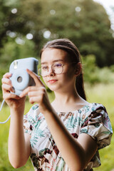 One cute girl is taking pictures with a camera in the park.