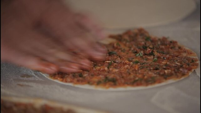 Spreading minced meat mixture on lahmacun dough, close-up static camera shot.