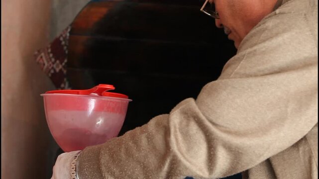 Traditional turnip juice producer filling plastic bottles using a funnel and a metal pot, side view, close up.