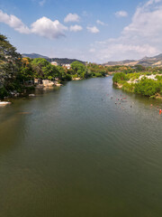 Fototapeta premium Drone perspective of people swimming in the scenic River Tecpan de Galeana, Guerrero, Mexico. Lush banks, distant mountains, clear sky.