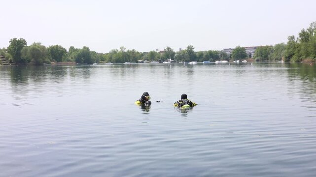 Professional scuba divers preparing for underwater operation in calm lake, safety and teamwork concept
