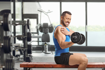 Fototapeta premium Man in a blue tank top feeling shoulder pain while lifting a dumbbell