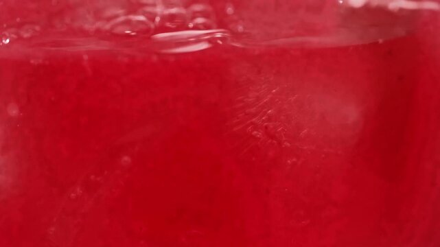 Macro Close-up of Fresh Red Berry Juice Pouring into Transparent Cup with Ice Cubes on Pink Background, Summer Cold Drink Commercial
