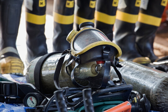 Firefighter Responds with Breathing Apparatus on Gray Tarp in Dark Setting, Wearing Protective Gear, Equipped with Firefighter Helmet and Scuba Mask, Ready for Rescue Operations