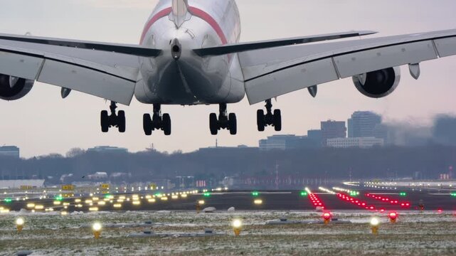 A large passenger airplane makes a dramatic landing on a snowy runway. The video shows the final approach, touchdown, and engine reverse thrust creating vapor in the cold winter air, filmed in slow