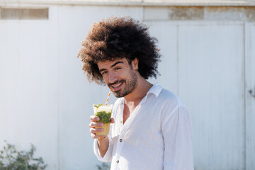 Young man smiling and drinking a mojito cocktail outdoors on a warm sunny day