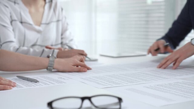 Business professionals reviewing contracts and paperwork in a meeting, pointing to key legal terms, negotiating and preparing signatures to finalize a collaborative agreement