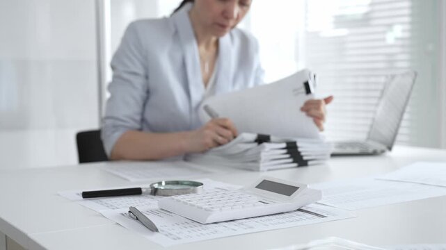 Business person working on financial documents, accounting or auditing a large stack of paperwork, managing tax forms and corporate reports with a pen at an office desk. Audit and taxes