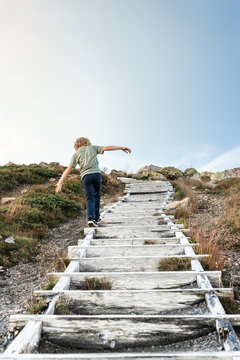 Child playing and balancing on a long wooden staircase in the mountains. Young boy exploring nature and testing his balance during a summer family adventure in scandinavia. authentic lifestyle.
