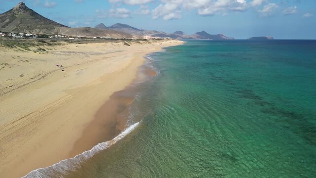 Aerial view of drone flying over golden sand beach with a small rock island in Porto Santo, Madeira, Portugal. Portuguese paradise with clean transparent water.