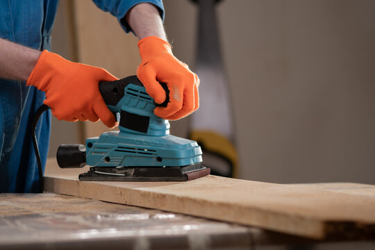 Close up carpenter hands using electric sander machine over wood. Woodworking and construction