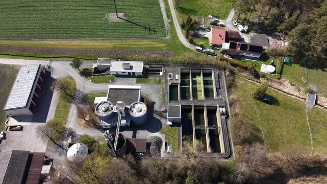 Aerial drone shot moving forward and tilting down into a top-down view over an abandoned water treatment facility with unused basins, green stagnant water, and industrial structures. Concept of infras