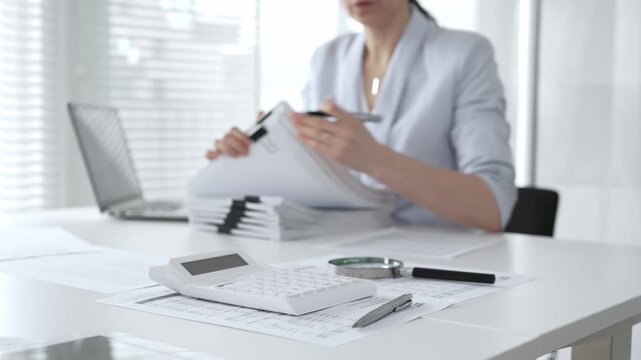 Business person working on financial documents, accounting or auditing a large stack of paperwork, managing tax forms and corporate reports with a pen at an office desk. Audit and taxes