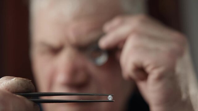 Senior man jeweler inspecting gemstone with jeweler loupe at closeup.