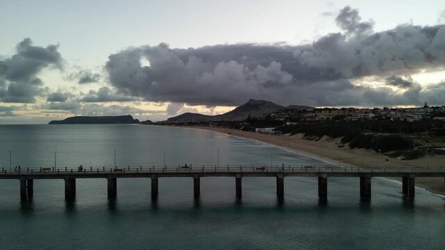 Aerial drone view of long golden sand beach of Porto Santo Island, Madeira, Portugal. Cloudy sunset. Port and small marina. Mountains in the background