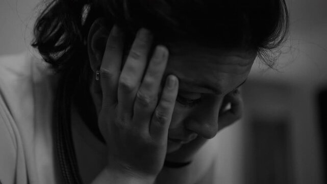 close up of woman holding head with hands showing emotional strain fatigue and mental overload intense moment of stress and inner pressure at home, black and white