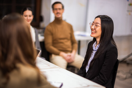Professional Asian woman explaining her qualifications during a job interview in a modern office.