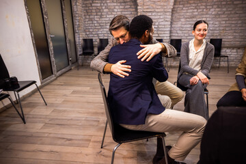 Two diverse colleagues hugging for support during a group therapy session in the office.