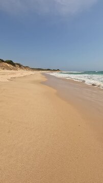 Vertical view first-person walking on the seashore golden sand of a paradisiacal beach with blue sky and turquoise water, in Bolonia Beach, Cadiz, Andalusia, Spain. Point Of View (POV), subjective vie