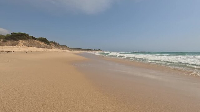 Wild paradise beach with golden sand and turquoise water, gentle waves breaking on the sea shore and blue sky. Bolonia Beach, Cadiz, Andalusia, Spain