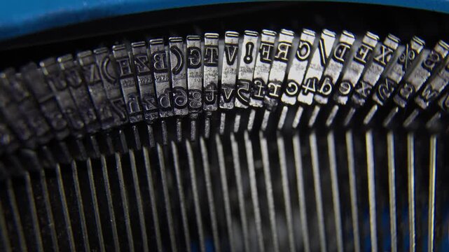 Close-up shot of a blue vintage typewriter's internal mechanism showing metal alphabet keys and typebars in motion.