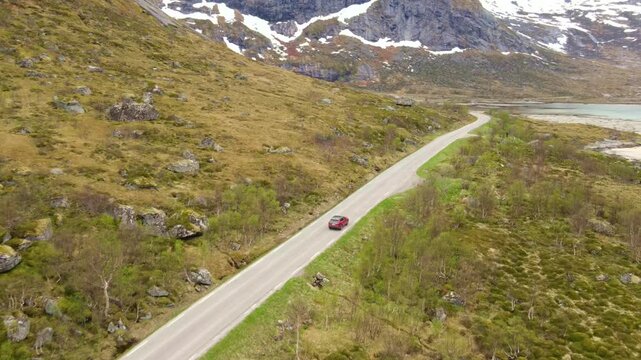 Aerial footage of a car driving along a road in Lofoten, Norway, on a cloudy day, drone footage, 4k 30fps