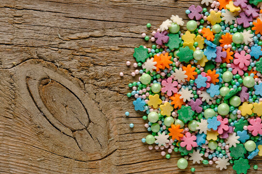 Decorative flower shaped sugar sprinkles and green pearls on an old wooden table, spring baking concept.