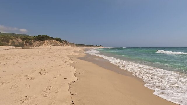 First-person view walking on the seashore golden sand of a paradisiacal beach with blue sky and turquoise water, in Bolonia Beach, Cadiz, Andalusia, Spain. Point Of View (POV), subjective view
