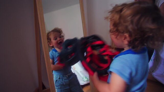 Toddler holding helmet and looking at reflection in mirror smiling playful childhood moment of self recognition and joyful exploration inside home environment