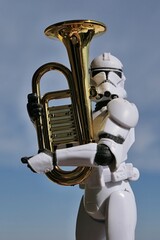 Naklejka premium Action figure of Star Wars clone trooper in white helmet and armor ready to play on a model of some kind of euphonium brass instrument, blue spring skies with overcast clouds in background. 