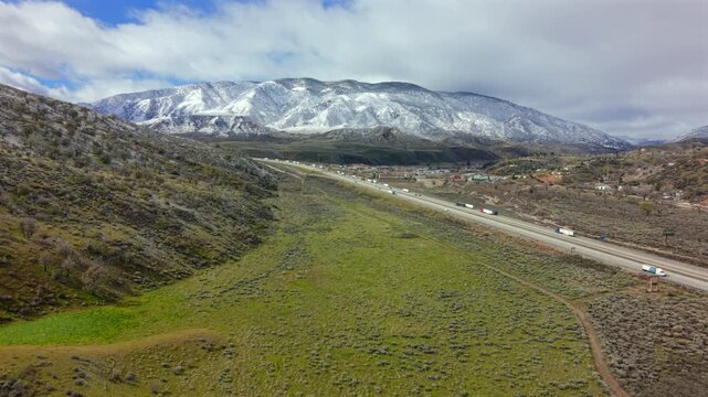 Aerial footage capturing car highway traveling through lush valley and rugged terrain. Overhead view illustrating transportation route winding through verdant landscape and mountainous region