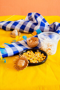 Traditional Festa Junina snacks and decorations with popcorn, corn, and straw hats on yellow background