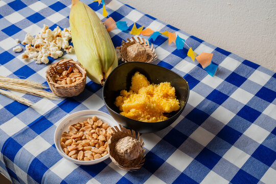 Traditional Festa Junina snacks with corn, popcorn, peanuts and cuscuz on blue checkered tablecloth