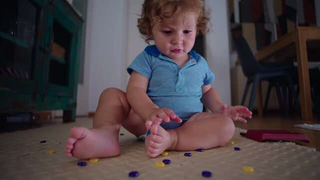 Toddler sitting on floor scattering small game tokens across living room mat while playing mischievously, playful childhood mess curiosity exploration and carefree home moment
