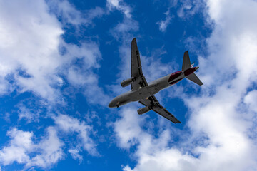 Fototapeta premium Airplane flying through a partly cloudy blue sky, showcasing the underside of the aircraft with visible engines and wings during daytime travel