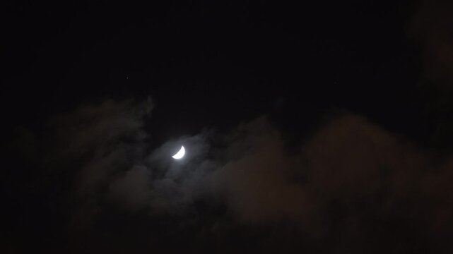 A cinematic view of the moon shining through clouds in the night sky.  tranquility, mystery, natural beauty, and nighttime atmosphere. 