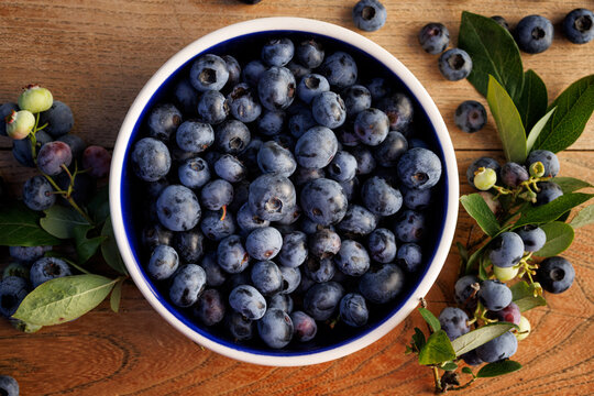 Fresh blueberries in a bowl on a wooden table, top view.