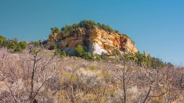 A wide shot of the dry, scrubby landscape and a large, layered sandstone mesa under a vibrant blue sky, captured along the East Mesa Trail in Zion National Park, Utah, USA.