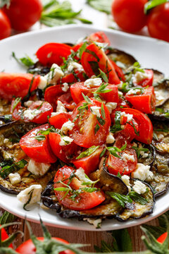 Salad of grilled eggplant slices with tomatoes and Feta cheese crumbled, drizzled with olive oil and seasoned with fresh herbs, close-up view