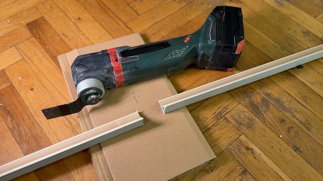 Cordless power tool with long guide rail rests on cardboard over a wooden floor, practical workshop mood for home improvement and renovation tasks