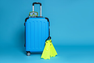 Suitcase, flippers and diving mask on light blue background. Space for text © New Africa