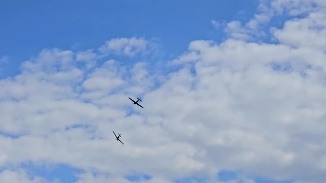 Pair of vintage propeller warbirds performing tactical maneuvers and aerial combat simulation in a cloudy sky.