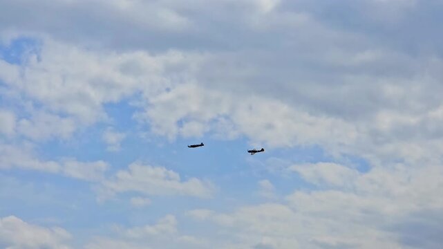 Pair of vintage propeller warbirds performing tactical maneuvers and aerial combat simulation in a cloudy sky.