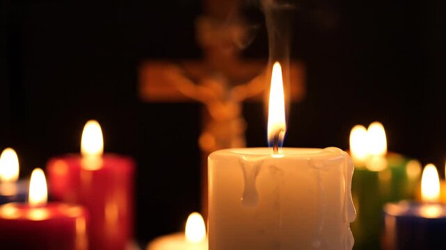 Burning white pillar candle with melting wax drips in close-up, background featuring a blurred wooden crucifix and various colored out-of-focus candles in a dark spiritual setting.